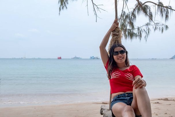 晴れた日には熱帯のビーチでのスイングでタイの女性の笑顔。アジアの女の子はビーチで楽しむ. - 写真・画像