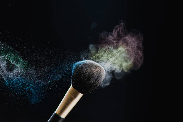 De kunst van het gelaat. Close-up foto van professionele zwarte make-up borstel met gekleurd poeder geïsoleerd op zwarte achtergrond - Foto, afbeelding