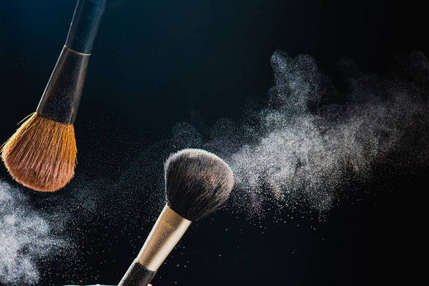 De kunst van het gelaat. Close-up foto van professionele zwarte make-up borstel met gekleurd poeder geïsoleerd op zwarte achtergrond - Foto, afbeelding