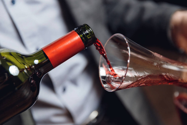 Giet rode wijn in glas tegen donkere achtergrond - Foto, afbeelding