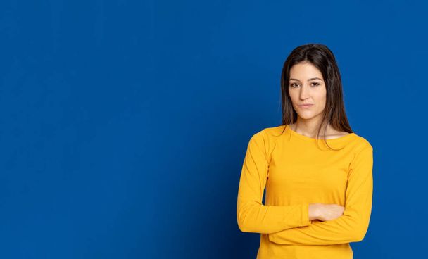 Esmer genç bir kadın, mavi arka planda sarı bir tişört giyiyor. - Fotoğraf, Görsel