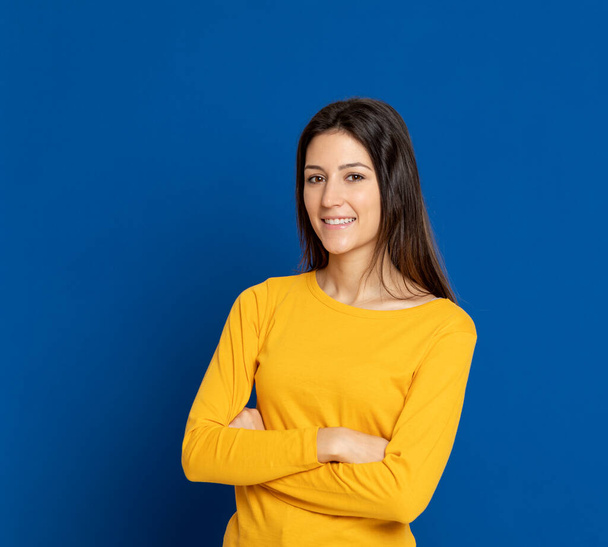 Brunette young woman wearing a yellow T-shirt on a blue background - Fotoğraf, Görsel