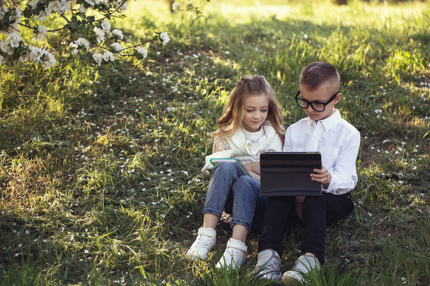 Two little Caucasian children wolk in the park with each other. Brother and sister spend time together. older brother help his younger sister with homework. Stylish clothes, cool glasses and happy faces - Foto, imagen