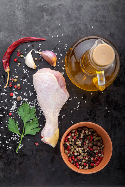 rauwe kippenpoot met specerijen en olijfolie in een fles, op een zwarte achtergrond, bovenaanzicht - Foto, afbeelding