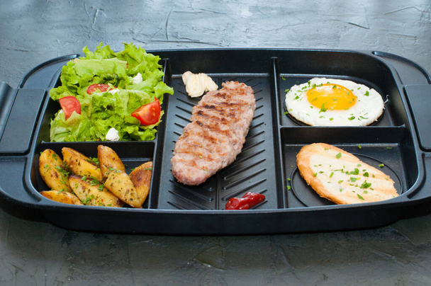 Завтрак, котлета или стейк, томатный салат, жареный картофельный крутон и жареное яйцо
 - Фото, изображение