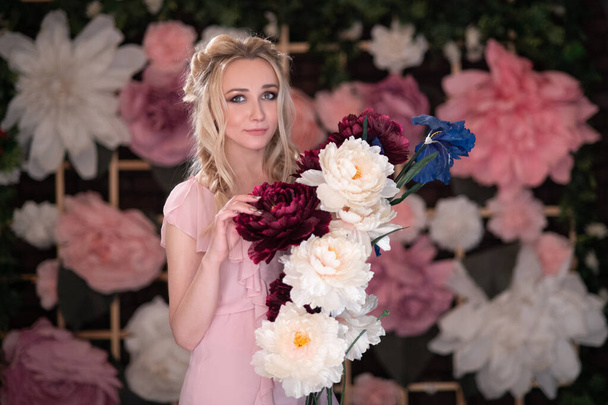 a blonde girl with 2 pigtails on the background of a flower wall with a sprig of large artificial flowers - Foto, immagini