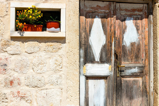 Hiteles ház kőfallal és gyönyörű ajtóval és virágcserépekkel a bejáratnál, minimális stílusban, élénk színekkel, háttérrel. Montenegró - Fotó, kép