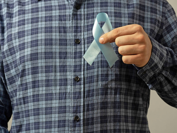 チェックされたシャツの男は前立腺癌の認識の彼の手印で青いリボンを保持する。医学と人間の健康の概念を閉じます - 写真・画像