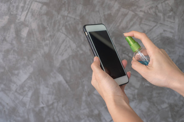 Closeup χέρια γυναίκα χρησιμοποιώντας ψεκασμού αλκοόλ απολυμαντικό οθόνη καθαρισμού smartphone, για την πρόληψη του ιού και των βακτηρίων. Καθαρό smartphone. μέτρα κατά του Covid-19. Έννοια υγιεινής: έννοια καθαρισμού. - Φωτογραφία, εικόνα