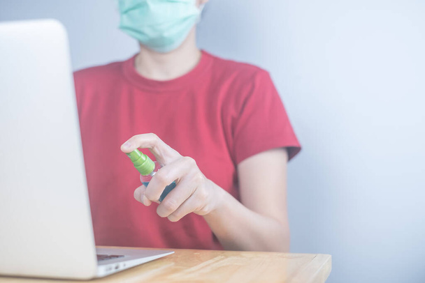 Asian woman wears protective mask using spray alcohol sanitizer cleaning a computer, to prevent the virus and bacterias. woman in quarantine for coronavirus.Cleaning her computer with spray alcohol - Photo, Image