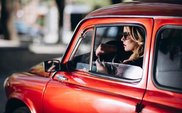 Femme blonde caucasienne en voiture rétro rouge conduisant la nuit dans le style James Bond
. - Photo, image