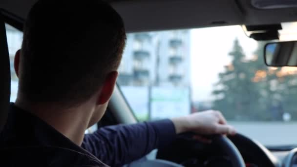 Młody człowiek w samochodzie. Radosny, przystojny kierowca siedzi na przednim siedzeniu, ogląda się za siebie i uśmiecha. Trzymaj ręce na kierownicy.. - Materiał filmowy, wideo