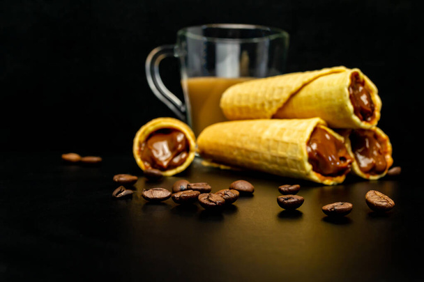 Hostienrollen mit Kondensmilch und einer Tasse Kakao auf schwarzem Hintergrund - Foto, Bild