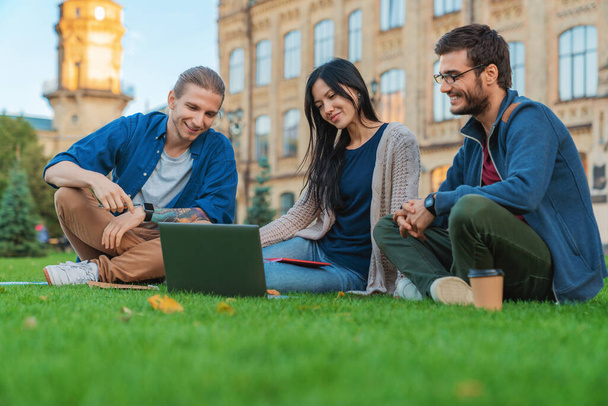 Students sitting on the grass near university while working on laptop - Photo, image