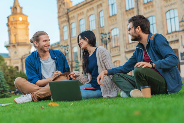 Heureux étudiants utilisant un ordinateur portable sur la pelouse du campus
 - Photo, image