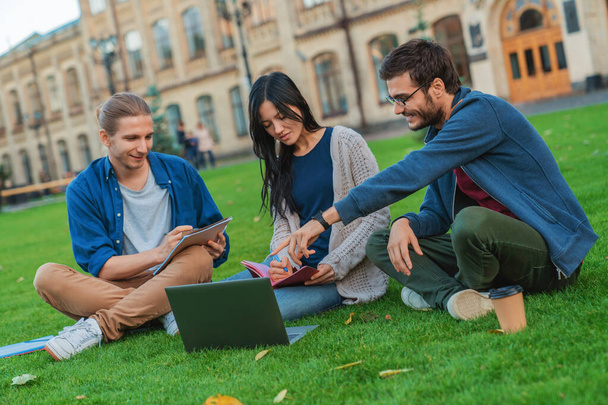 Groep jonge studenten die samen laptop gebruiken in het park bij de universiteit - Foto, afbeelding