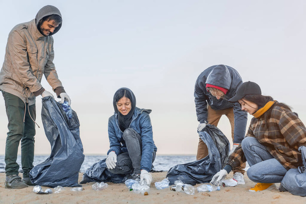 Young man picking up trash and plastic with group of volunteers on the beach - Φωτογραφία, εικόνα