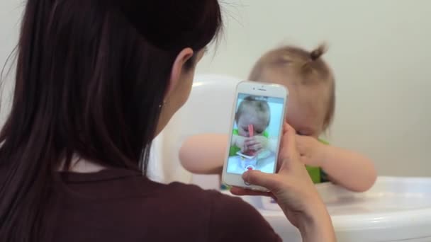 Anne, bebeğin akıllı telefon kullanıp fotoğraf çekerken, bebeğin sosyal medyada annelik yaşam tarzını paylaşırken eğlenirken çekilmiş fotoğrafı ve videosu var. Kız ilk kez yemek yiyor. - Video, Çekim