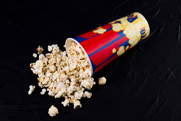 Tasty popcorn spilled from a overturned box dark background. - Fotó, kép