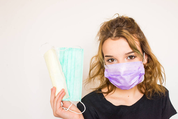Charming girl wearing protective medical face mask for coronavirus protection. Female teenager in mask holds two medical face masks in hands. Mask assortment. Wearing a mask for hygienic reason. - Photo, Image