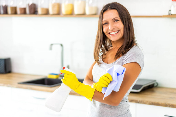 Woman with obsessive compulsive disorder cleaning kitchen with detergents, but everything is clean anyway. - Foto, Bild