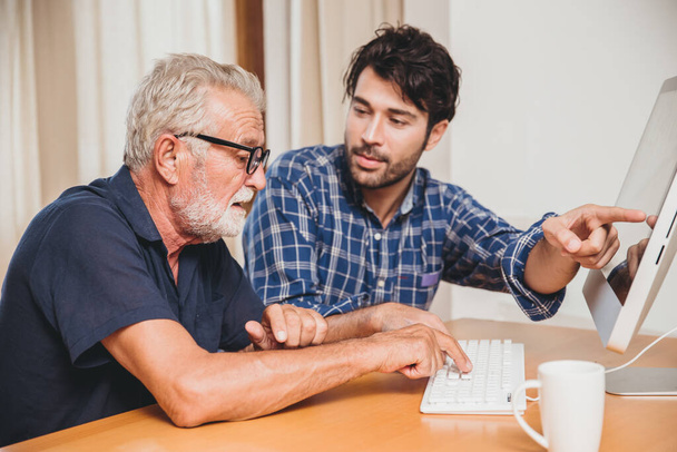 młody mężczyzna lub syn uczy dziadka starszego ojca korzystania z komputera w domu. - Zdjęcie, obraz