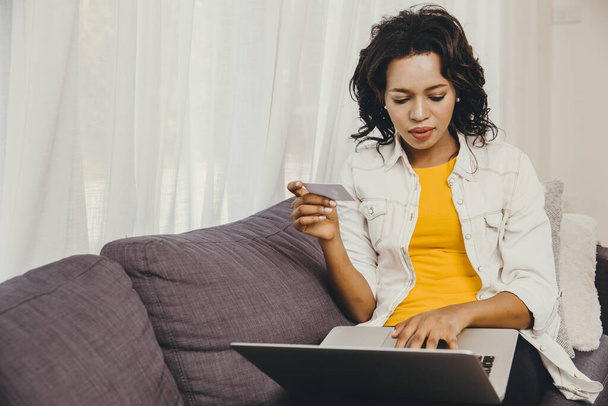 Siyah Afro-Amerikalı bir kadın, evde kaldığı süre boyunca dizüstü bilgisayardan yeni bir şey almak için kredi kartı kullanıyor.. - Fotoğraf, Görsel