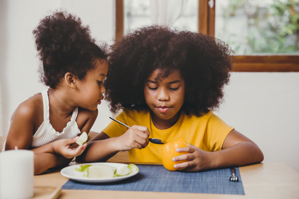 Маленькая милая младшая сестра выглядит интересно ее старшая сестра пытаются научиться есть овощи
. - Фото, изображение