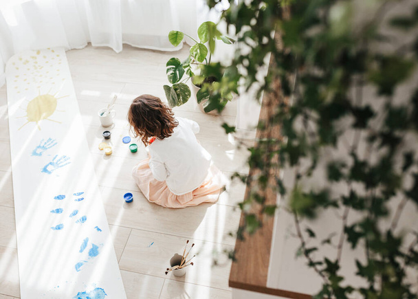 Roztomilá šťastná holčička, rozkošná předškolačka, malování s barvami na papírové role sedící na podlaze ve slunném bílém obývacím pokoji doma, kreativní mladý umělec v práci - Fotografie, Obrázek