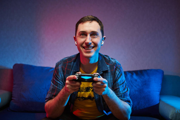Ritratto di pazzo giocoso Gamer godendo la riproduzione di videogiochi su Playstation al chiuso seduto sul divano, tenendo Console Gamepad in mano, fan di Xbox. Riposare a casa, avere un grande Weekend
. - Foto, immagini