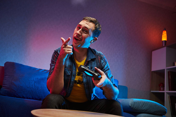 Portret szalonego, zabawnego gracza, bawiącego się graniem w gry wideo na PlayStation w pomieszczeniach, siedzącego na sofie, trzymającego w rękach Gamepad konsoli, fanów konsoli Xbox. Odpoczywaj w domu, miłego weekendu.. - Zdjęcie, obraz