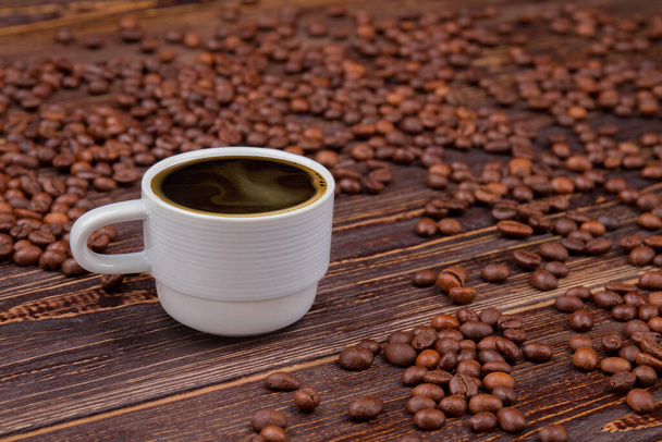 Kopje koffie en verstrooide koffiebonen op tafel. - Foto, afbeelding