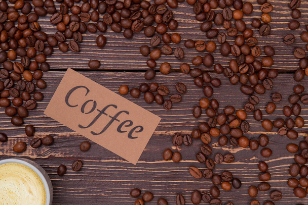 Πολλοί κόκκοι καφέ και φλιτζάνι καφέ με αφρό. - Φωτογραφία, εικόνα