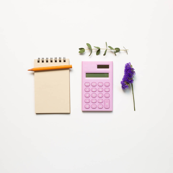 Lugar de trabajo y estudio, cuaderno y calculadora digital y lápiz con flor seca sobre fondo blanco. plano, vista superior, espacio para copiar
 - Foto, imagen