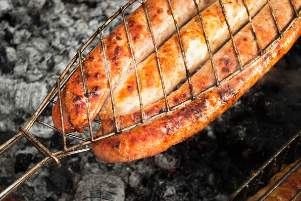 Мясо-сосиски, жареные в сетке над огнем. Барбекю на открытом воздухе летом
. - Фото, изображение