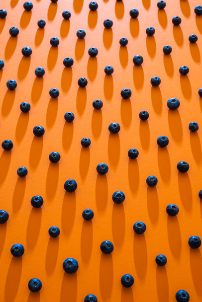 Organic blueberries symmetrically aligned on a seamless orange background. Funny pattern with blueberry beads. Ripe summer fruits background. - Photo, Image