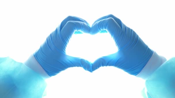 Ręce lekarza w niebieskich rękawiczkach tworzą serce na tle lampy operacyjnej. Pielęgniarka wykazuje oznaki miłości podczas pandemii. Lekarze ratują ludzi. Dowódca-19. Koronawirus - Materiał filmowy, wideo