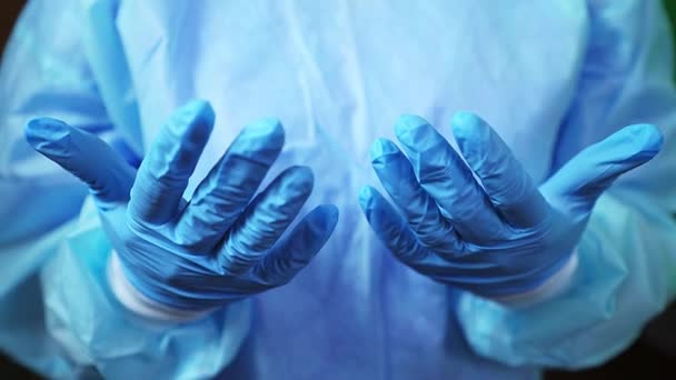 Dokter in blauwe medische handschoenen en een beschermend pak. Handen van een verpleegster die mensen redt tijdens een epidemie. Vermoeide handen van een medische professional. Bescherm uw handen tegen virussen. Wereldpandemie - Video