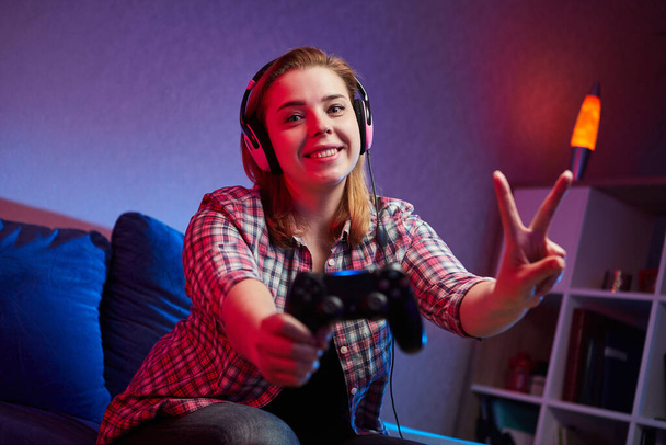 Портрет сумасшедшего игривого геймера, девушка наслаждается игрой в видеоигры в помещении, сидя на диване, держа в руках консольный геймпад. Отдых дома, отличных выходных
 - Фото, изображение