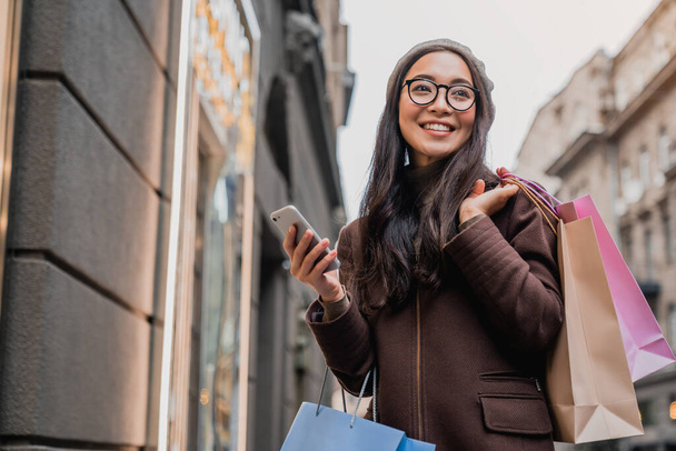 Asian woman using smartphone and looking away while enjoying a day shopping - Foto, immagini