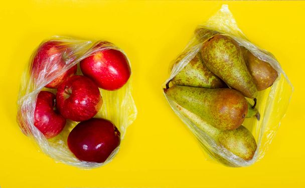 Ecology concept: fruits (red apples and green pears) in two plastic bags on yellow backround. Top veiw. - Photo, Image