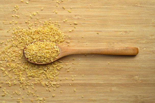 Сухая треснувшая пшеница далия зерна в деревянной ложке, на бамбуковой разделочной доске - Фото, изображение