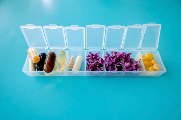 Le capsule si trovano in una scatola pillola su uno sfondo blu. Scatola per imballaggio compresse per una settimana. Medicina e fiori, medicina alternativa
 - Foto, immagini