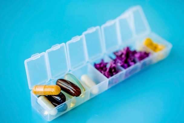 Le capsule si trovano in una scatola pillola su uno sfondo blu. Scatola per imballaggio compresse per una settimana. Medicina e fiori, medicina alternativa
 - Foto, immagini