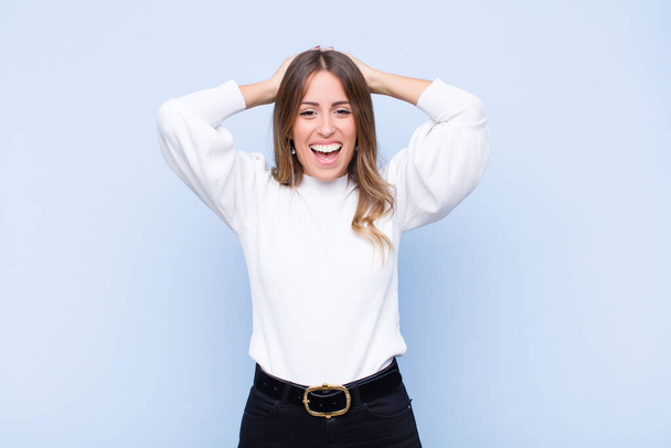 young pretty hispanic woman looking happy, carefree, friendly and relaxed enjoying life and success, with a positive attitude against blue wall - Foto, afbeelding