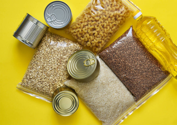 Food donations on a yellow background: oil, buckwheat, sugar, canned food. Sit at home. Quarantine. - Photo, Image