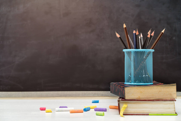 Back to school and education concept. Books with pencil holder on white table. blackboard in background.  - Photo, Image