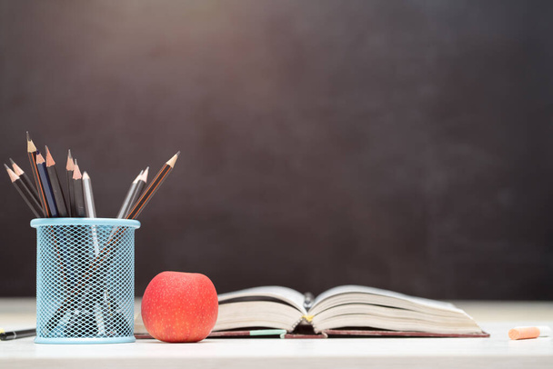 Вернемся к школе и концепции образования. Подставка для карандашей с красным яблоком на белом столе. доска в фоновом режиме
. - Фото, изображение