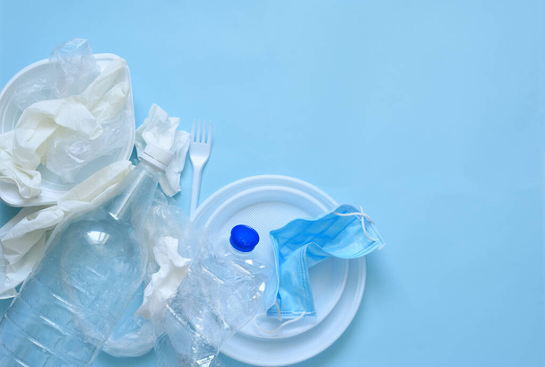 Plastic trash on a blue background: plates, bottles, polyethylene, mask. Environmental pollution. Ecological disaster. - Foto, imagen