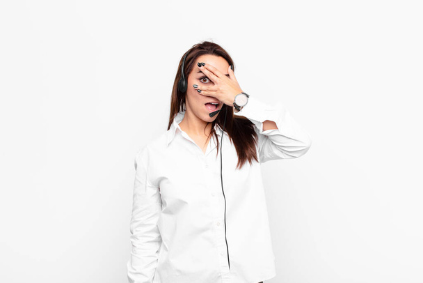 young pretty woman looking shocked, scared or terrified, covering face with hand and peeking between fingers with headphones and microphone - Photo, Image